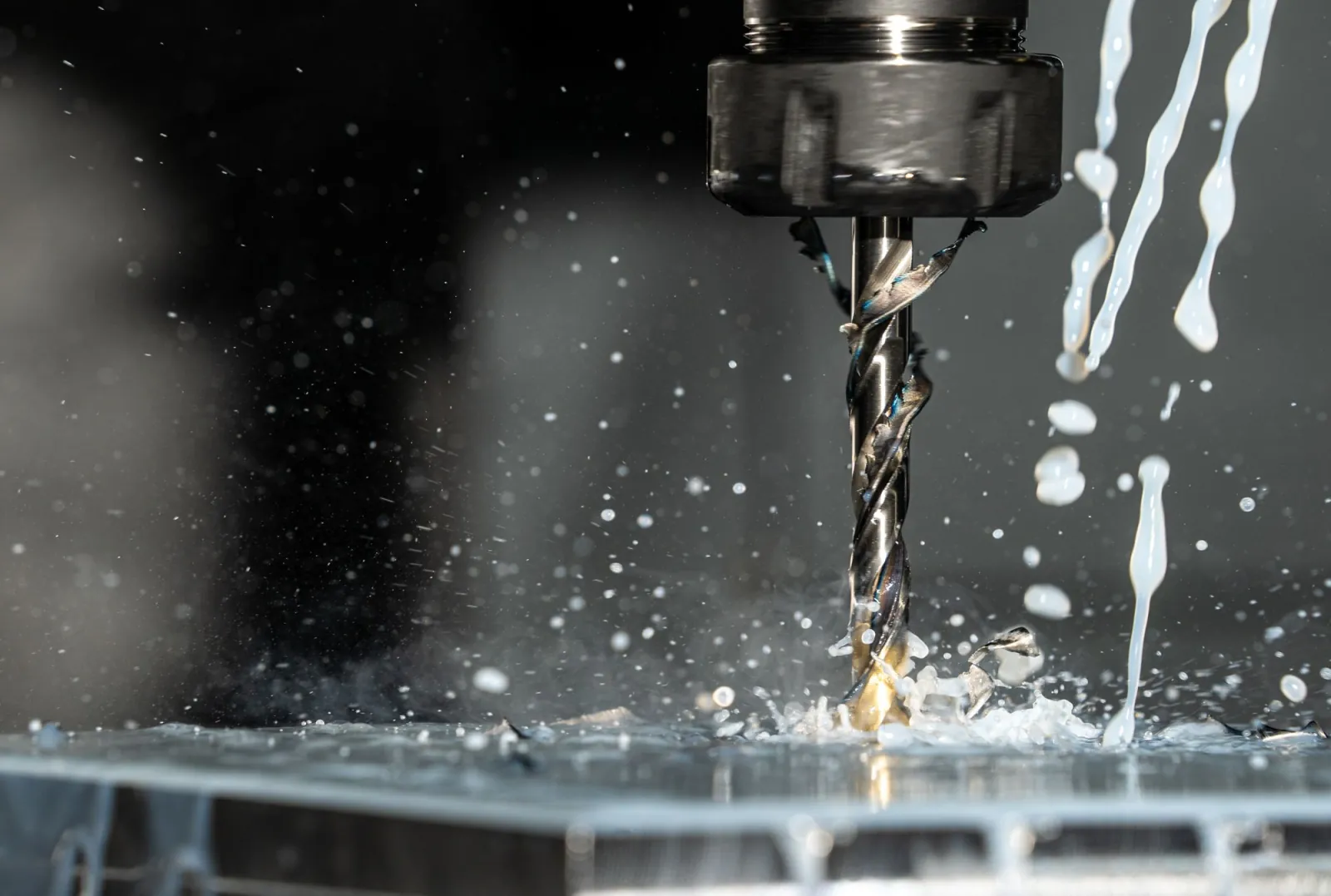 A drill bit cutting into metal under a spray of coolant